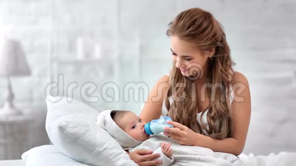 微笑美丽的母亲从牛奶瓶中喂小婴儿享受母性视频的预览图