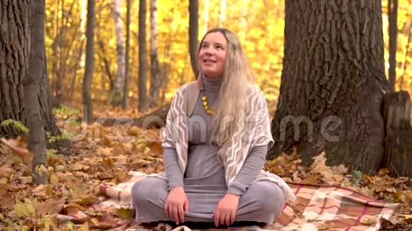 一位孕妇正坐在秋林中的一棵树下黄色的叶子在飘落慢动作视频的预览图