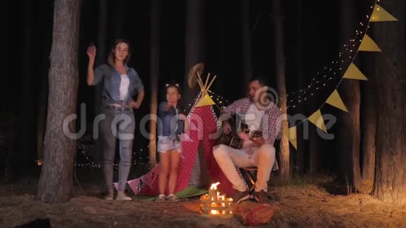 无忧无虑的童年美丽的女孩和她慈爱的母亲跳舞听父亲在晚上弹吉他的音乐视频的预览图