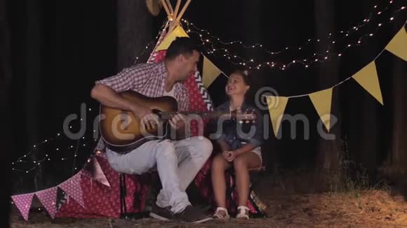 与父母放松美丽的卷曲女孩与父亲交谈和弹吉他在森林聚会上玩得很开心视频的预览图