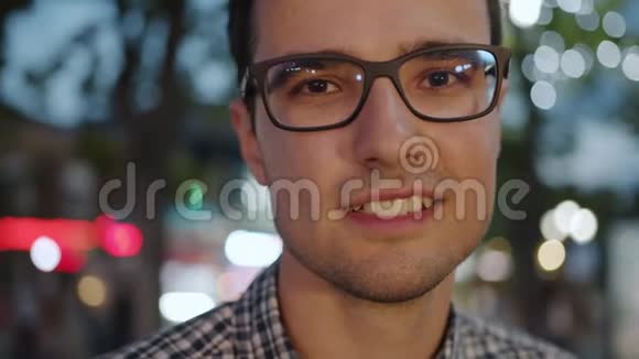 晚上戴着眼镜站在户外的快乐的黑发年轻人的特写照片视频的预览图
