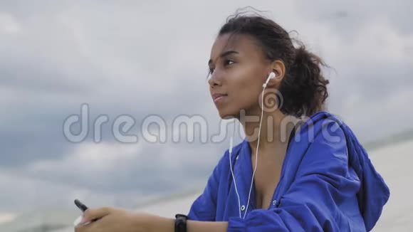 穿着运动服带耳机听手机音乐的女人在公园锻炼之间视频的预览图