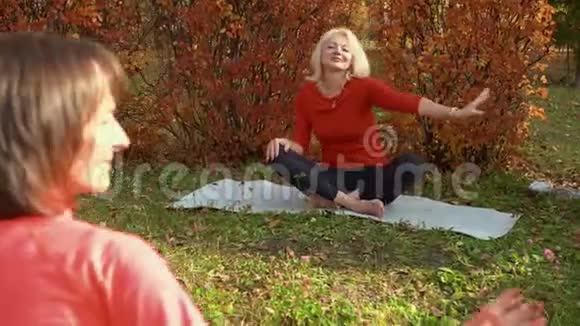 瑜伽女人在秋季公园冥想户外瑜伽训练在公园地毯上练习瑜伽体式的轻松女人视频的预览图