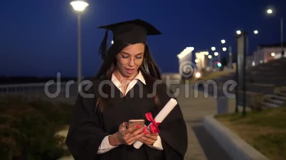 大学毕业生女孩带着文凭微笑使用她的智能手机视频的预览图