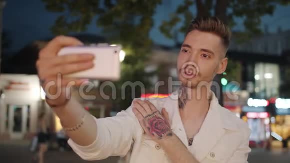 有纹身的年轻人在夏天晚上用智能手机在户外自拍视频的预览图