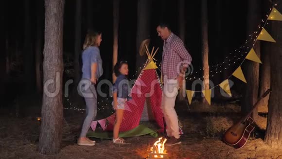 家庭度假时快乐的父母和快乐的女儿一起在森林野餐时一起跳舞露营视频的预览图