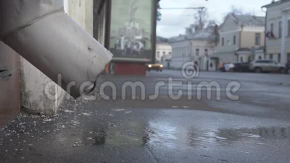 屋顶上的水在城市柏油路的排水管上滴落视频的预览图