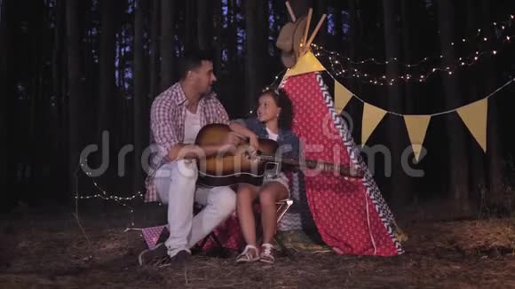快乐的家庭喜欢露营小女孩唱歌学弹吉他坐在爸爸身边背景是视频的预览图