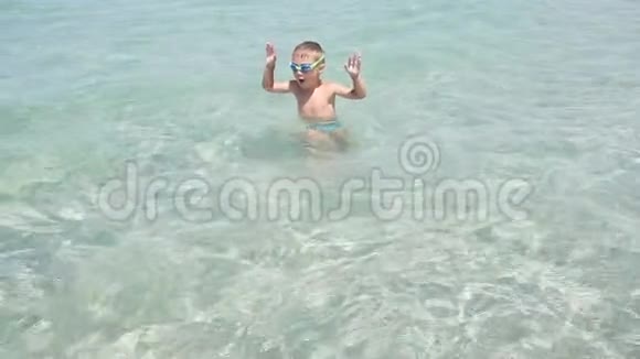 快乐的小男孩在一个温暖的阳光明媚的日子里快乐地跑着跳着在夏天的海水中溅起水花视频的预览图