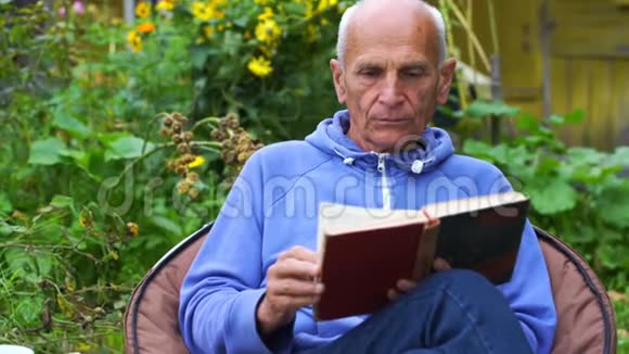 老人读书反对花园里盛开的花朵视频的预览图