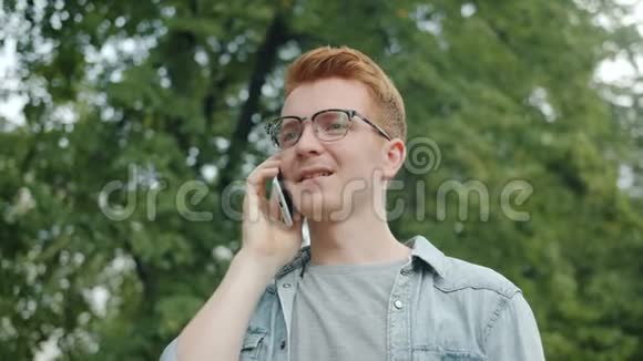 有魅力的商人戴眼镜在城市公园的户外用手机说话视频的预览图