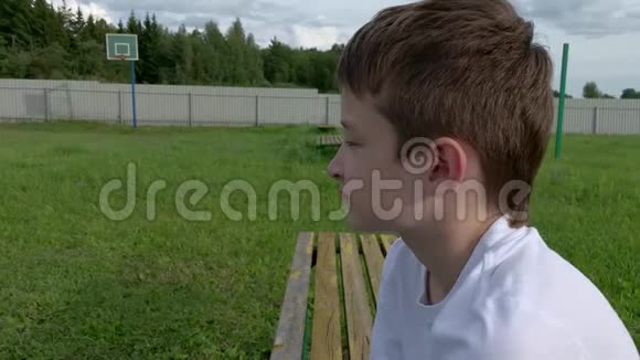 晚上一个孤独无聊的十几岁男孩坐在篮球场上的长凳上蚊子飞了很多视频的预览图