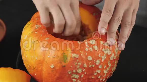 准备在万圣节制作灯笼用手在木桌上从一个橙色南瓜中舀取百事可乐种子视频的预览图