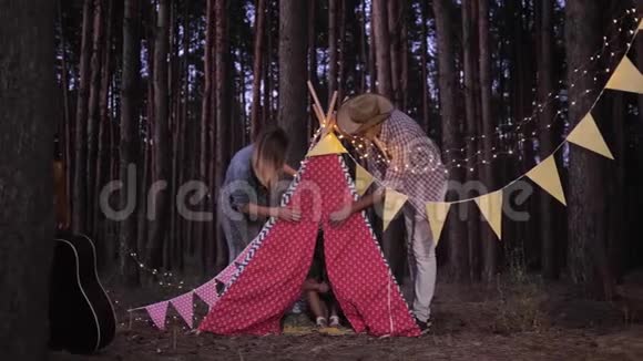 在晚上的森林露营旅行中小女孩躲在wigwam里爸爸妈妈很惊讶视频的预览图