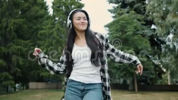 快乐的亚洲学生戴着无线耳机在户外跳舞视频的预览图