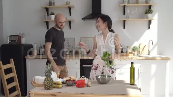 年轻快乐的丈夫拥抱微笑的妻子切菜色拉厨房深情的夫妇做饭说笑视频的预览图