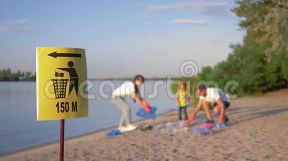 垃圾桶上的路标带小孩的年轻家庭在肮脏的沙滩上用塑料收集垃圾视频的预览图