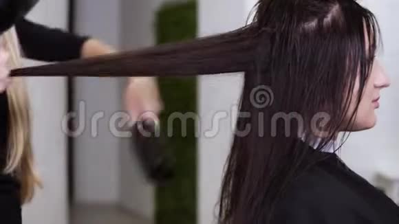 女理发师烘干坐在沙龙椅上的女性深色长发带有风扇和毛刷的理发器视频的预览图