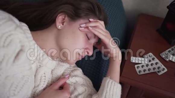 一个发烧头痛的病妇躺在床上看着药丸和药物的包装强烈的偏头痛和视频的预览图