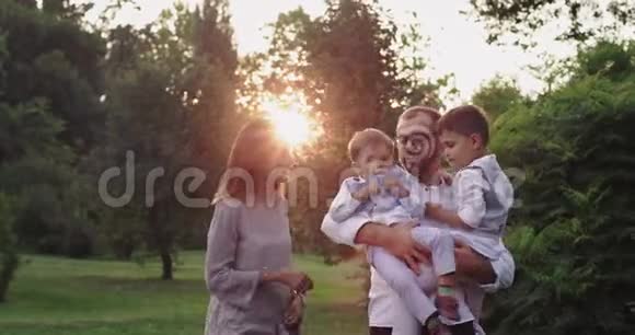 一个年轻的家庭带着两个孩子一起在绿色公园的中央尽情享受时光微笑着拥抱着跳跃着视频的预览图