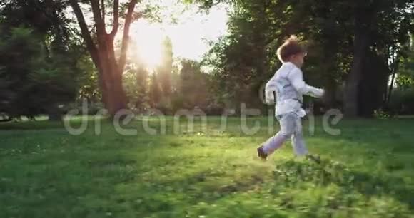 一个穿着西装风趣地在公园的草地上跑来跑去的帅气男孩在镜头前微笑着视频的预览图