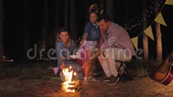 在森林里休息年轻的父母带着快乐的孩子在森林里野餐时用火煎棉花糖视频的预览图