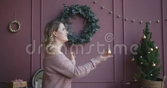 穿着毛衣的漂亮女人慢慢地举起一个圣诞球装饰圣诞树舒适的新年家视频的预览图