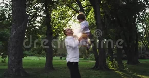 在一个绿色公园的中央爸爸抱着他的儿子一起转过身来享受着度过的时光视频的预览图