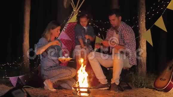 快乐的童年可爱的小女孩和她慈爱的父母在森林的篝火上玩着煎棉花糖的游戏视频的预览图