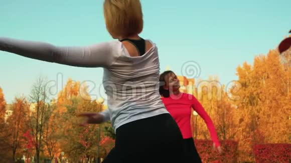 年轻女子一起在秋季公园训练瑜伽锻炼教练苗条的女人练习户外健身运动视频的预览图