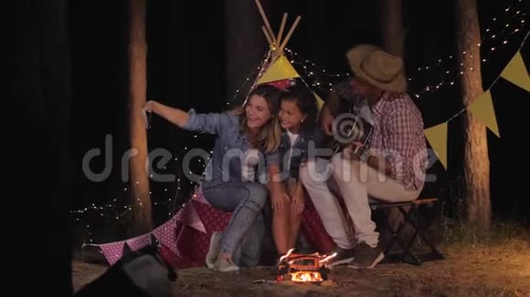 幸福的妻子和心爱的丈夫和美丽的女儿在wigwam和篝火的背景下自拍视频的预览图
