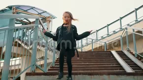 穿黑色皮夹克的少女在城市背景下走下楼梯穿皮夹克的摇滚女孩视频的预览图