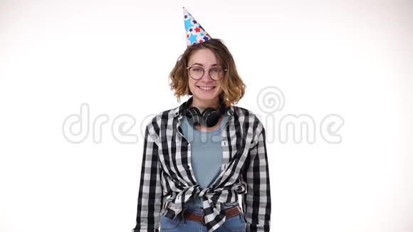 兴奋的年轻女子穿着格子衬衫戴着耳机戴着生日礼物戴着五颜六色的帽子吹着烟斗飘落下来视频的预览图