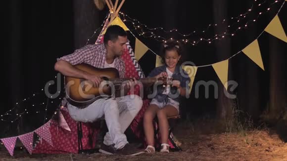 父亲和女儿会弹吉他周末在户外以wigwam为背景给妈妈打电话视频的预览图