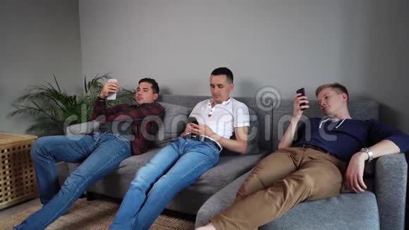 男人公司的三个朋友正在软沙发上使用电话视频的预览图