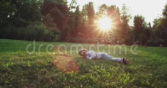 有魅力的小男孩两岁摔倒在绿草上直视着镜头笑得很可爱视频的预览图