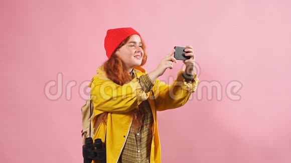 一个穿黄色斗篷的旅游女孩在智能手机上拍摄大自然的工作室肖像视频的预览图