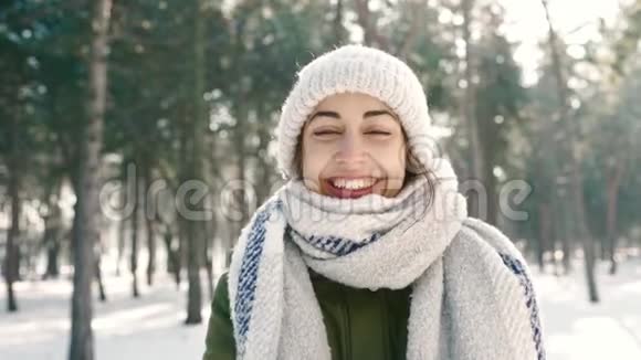 可爱的帽子和温暖的长围巾的滑稽微笑女人的特写镜头把雪扔到镜头前白雪皑皑的冬季公园视频的预览图
