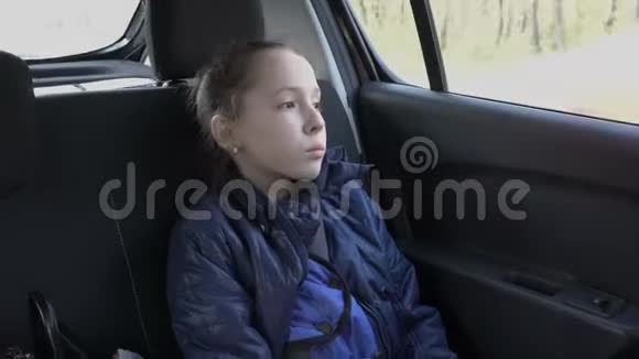 一个悲伤的小女孩沉思地看着天空和一辆驾驶汽车的窗户上的路她坐在后面视频的预览图