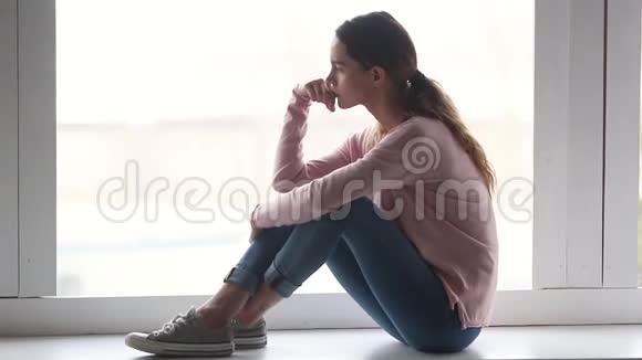 坐在窗台上的可怜的女人望着别处思考视频的预览图