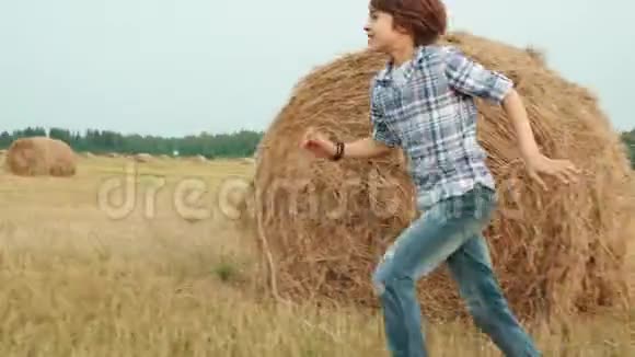 十几岁的男孩在干草堆背景下奔跑在农田里少女们坐在干草堆上收割田野视频的预览图