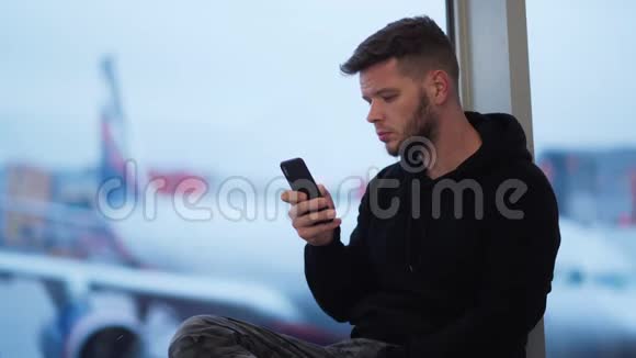 年轻人坐在机场用电话背景模糊的飞机视频的预览图