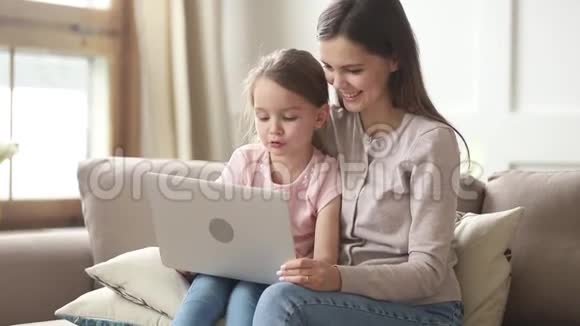 母亲坐在沙发上女儿为教育目的使用笔记本电脑视频的预览图