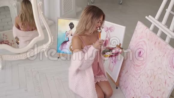 穿着粉红色针织毛衣的女孩在画室的帆布上画花视频的预览图
