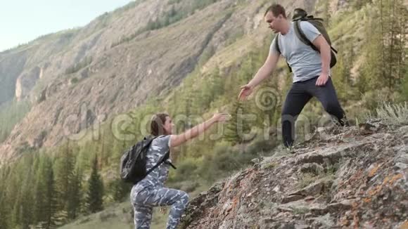 帮助两个登山者两个游客在山顶上一个男人帮助一个女人爬上一块陡峭的石头相互交流视频的预览图