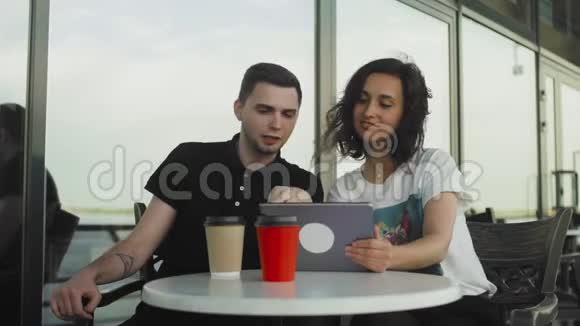 一家咖啡馆里的年轻男女看着他们在平板电脑上拍照聊天视频的预览图
