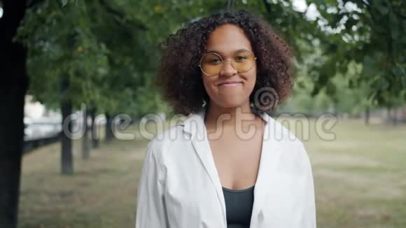 美丽的混血女郎在城市公园的户外微笑着展示好的手势视频的预览图