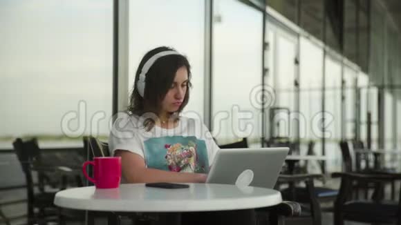带着耳机在咖啡馆工作的年轻女学生带着笔记本视频的预览图