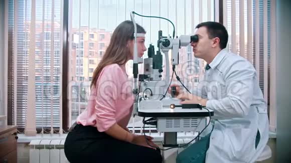 眼科医生医生正在用一种特殊设备检查穿着粉色开襟羊毛衫的视力女性视频的预览图