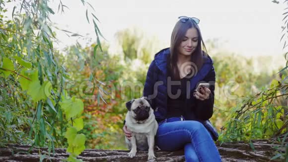 女孩和一只小狗坐在公园里用电话看新闻上网交流视频的预览图